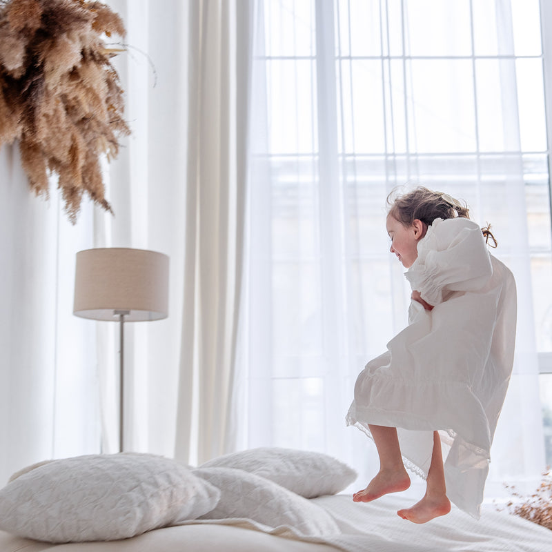 Kind speelt op bed in een licht slaapkamerinterieur; een goede huisstofmijt stofzuiger helpt allergieën voorkomen in kinderkamers